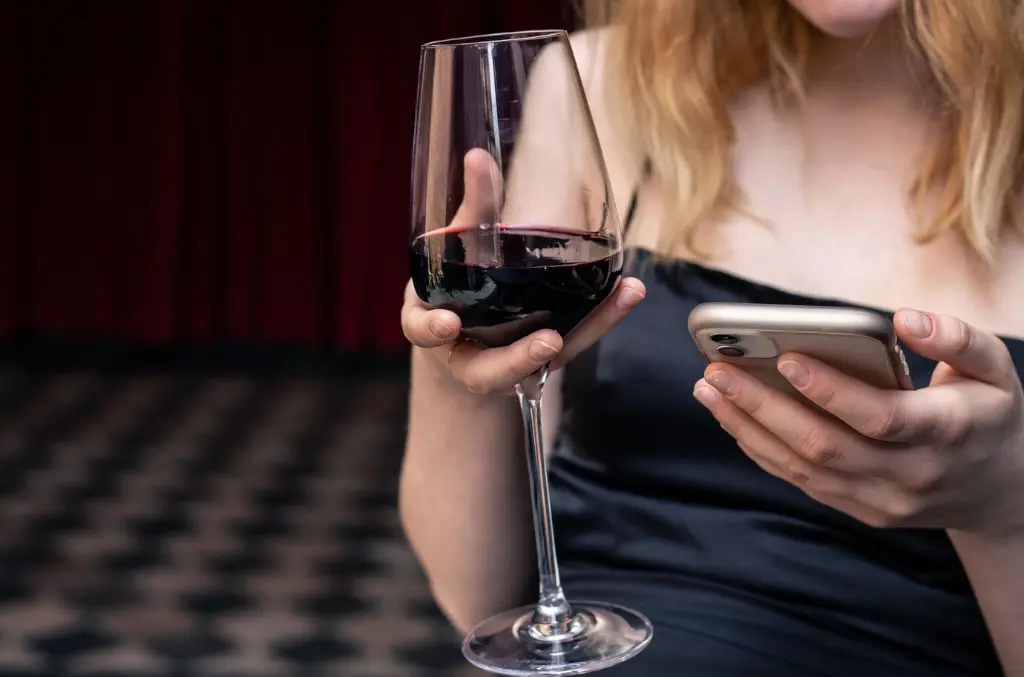 front view woman drinking red wine glass holding smartphone
