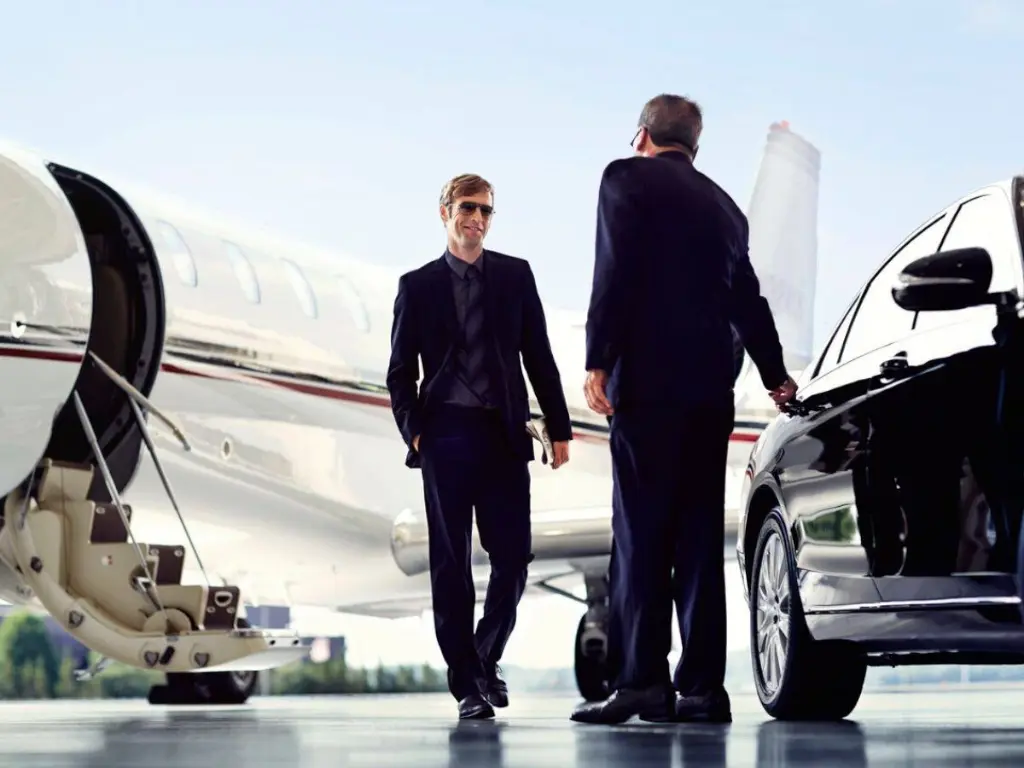 private jet man black suit chauffeur opening door luxury car tarmac hangar airport