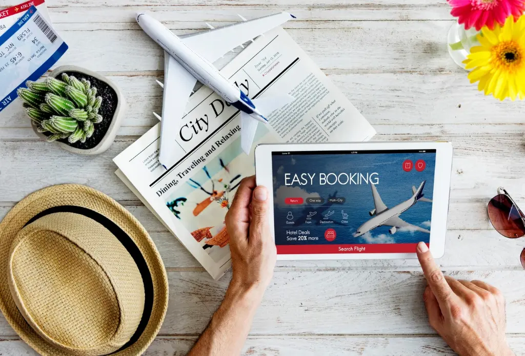 wooden table hat glasses tablet booking website woman hands newspaper cactus flight tickets flowers