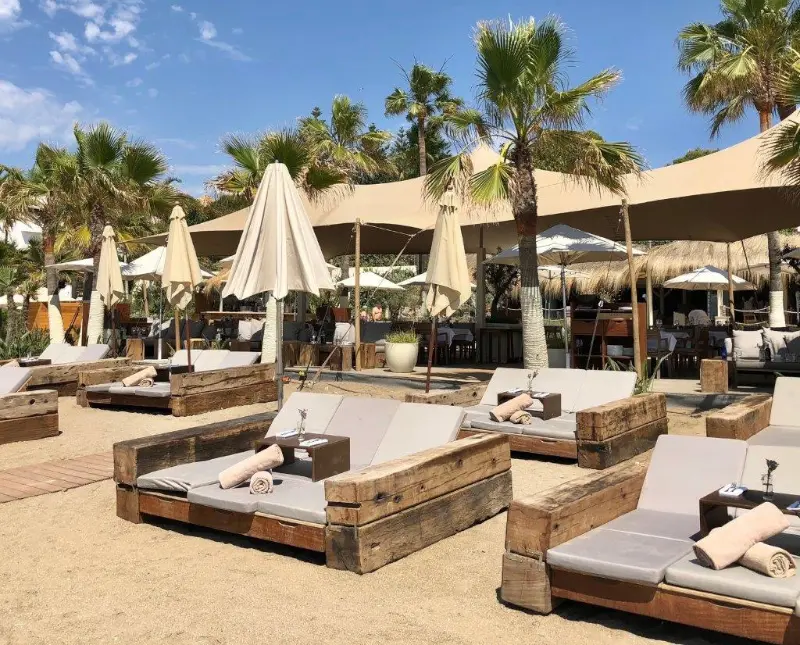 Vista frontal hamacas, sobrillas, palmeras y arena del Hotel Nobu en Marbella dia soleado